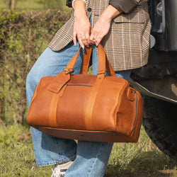 Person holding a cognac leather bag outdoors near a vehicle