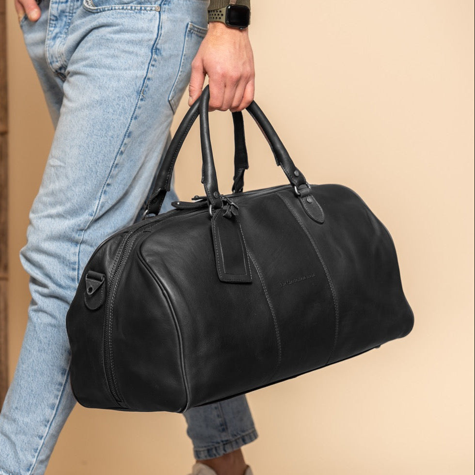 Person holding a black leather duffel bag with a neutral background