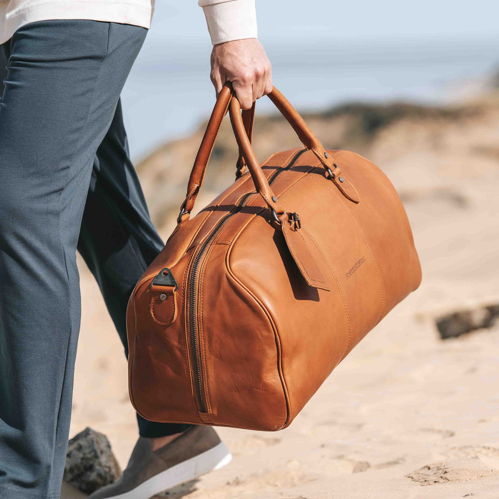 Person holding a cognac leather duffel bag on a beach