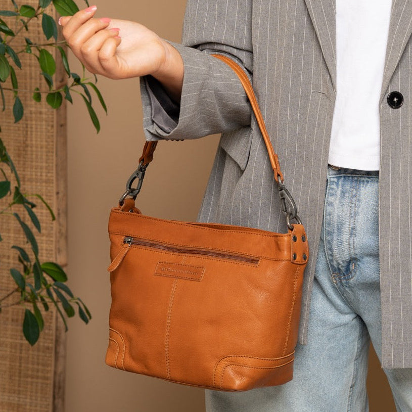 Person wearing a gray pinstripe blazer holding an cognac handbag against a beige background