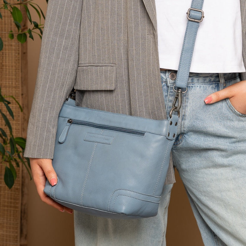 Person wearing a gray pinstripe blazer and light blue jeans, holding a blue handbag against a beige background.