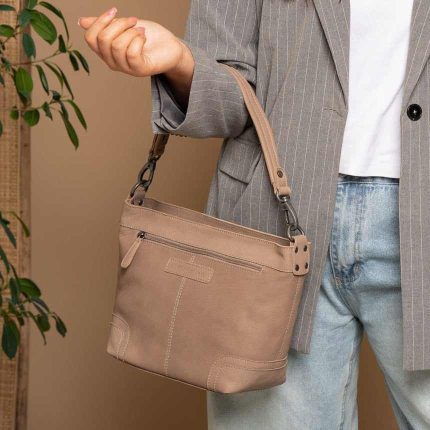 Person wearing a gray pinstripe blazer and light blue jeans, holding a soft pink handbag against a beige background.