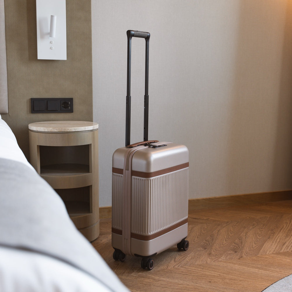 Beige suitcase with brown band on a wooden floor in a room.