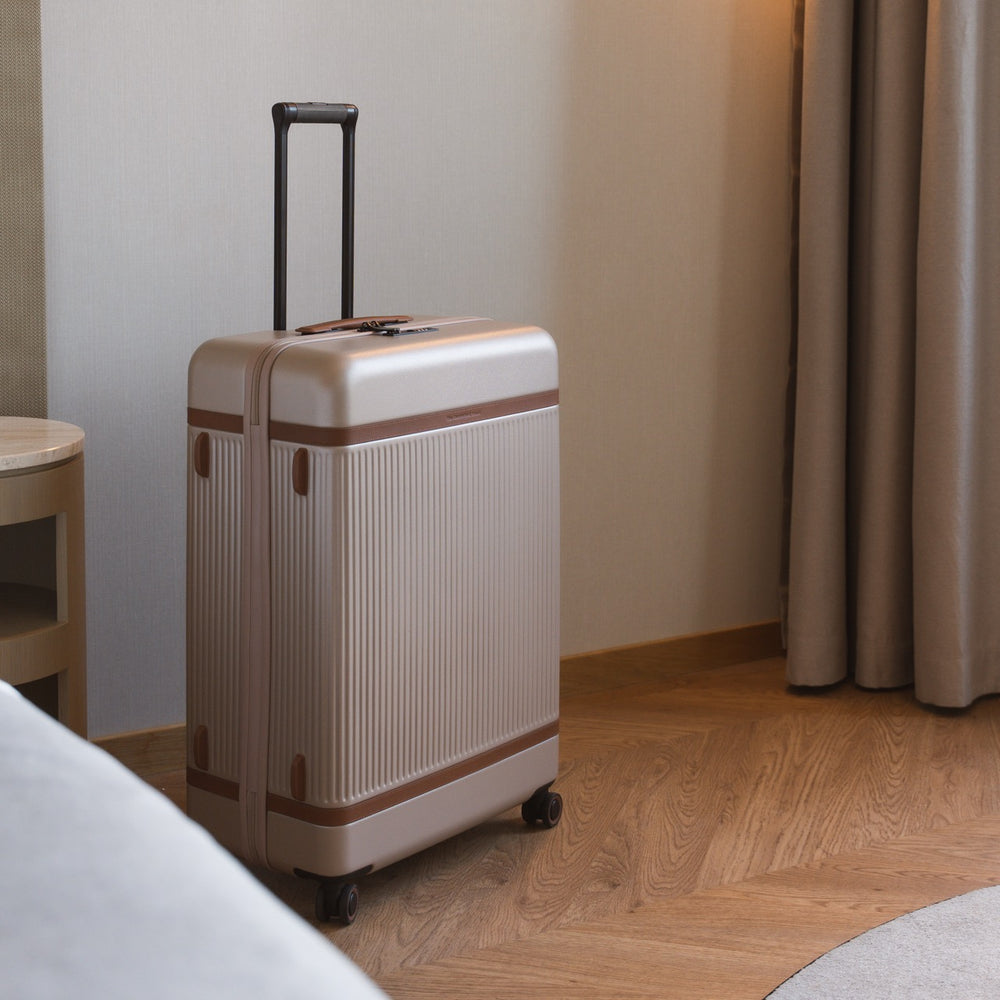 Beige suitcase with brown accents on a wooden floor in a room.