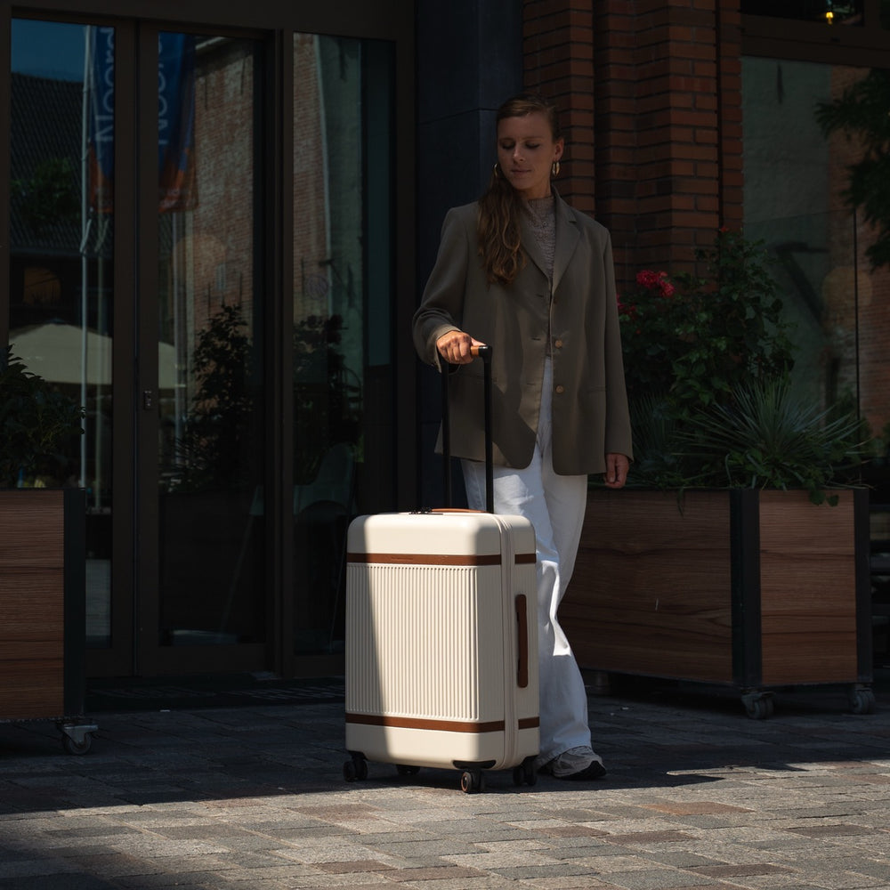 Woman pulling a suitcase on a sidewalk with a building in the background