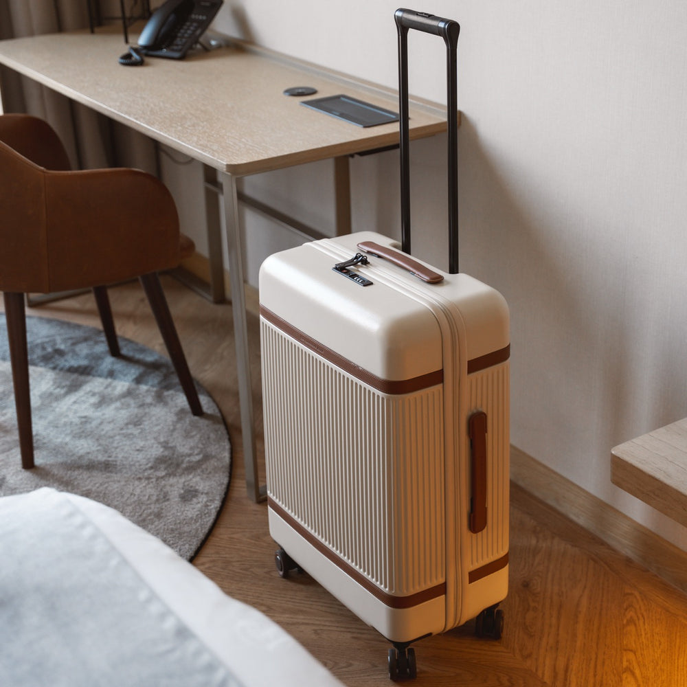 Off white suitcase with brown accents on a wooden floor next to a desk in a room.