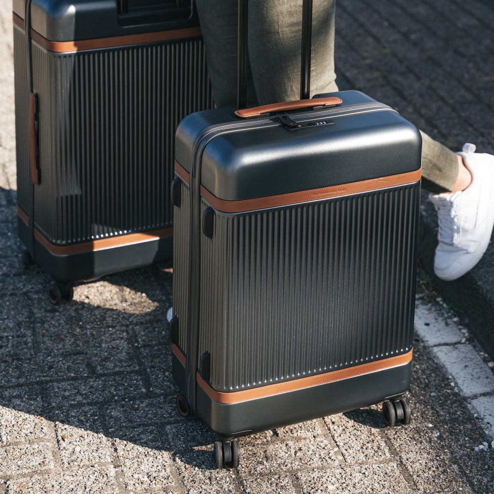 Two dark grey suitcases with brown accents on a paved surface.