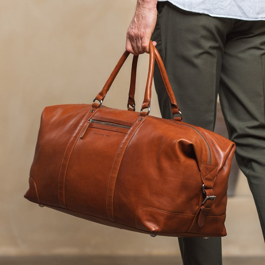 Person holding a cognac leather duffel bag in a neutral setting