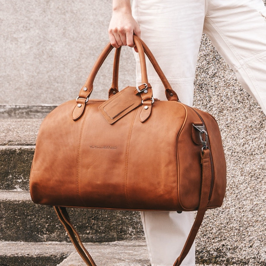 Person holding a cognac leather duffel bag on steps.