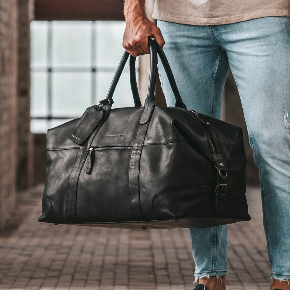 Person holding a black leather duffel bag in an urban setting.